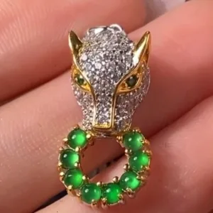 A hand delicately holds a Green Jade Pendant with Silver Inlay, showcasing a detailed fox head design with sparkling stones and golden accents. The fox's neck is adorned with a circle of luminous green jade beads set in a gold-tone base, creating an aura of elegance and mystery. The intricate craftsmanship and vivid colors of the pendant make it a captivating accessory.