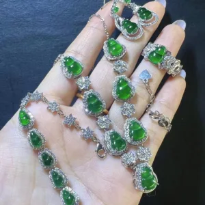 The image captures a hand holding a luxurious Jadeite Gourd Necklace. The necklace features multiple gourd-shaped jadeite charms with a deep green luster, each surrounded by a halo of twinkling stones set in silver. The charms are connected by a silver chain with additional star-shaped silver and stone accents, creating a continuous flow of elegance and harmony.