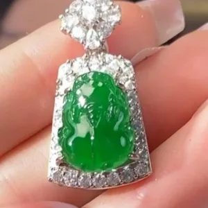The image displays a meticulously crafted Jadeite Sun Green Pixiu pendant, held between fingers. The pendant is distinguished by its bright green jadeite carving of a Pixiu, a mythical creature associated with wealth, encased in a radiant silver inlay adorned with glittering stones. The combination of the vivid green jade and the sparkling silver creates a piece that is both visually stunning and rich with cultural significance.