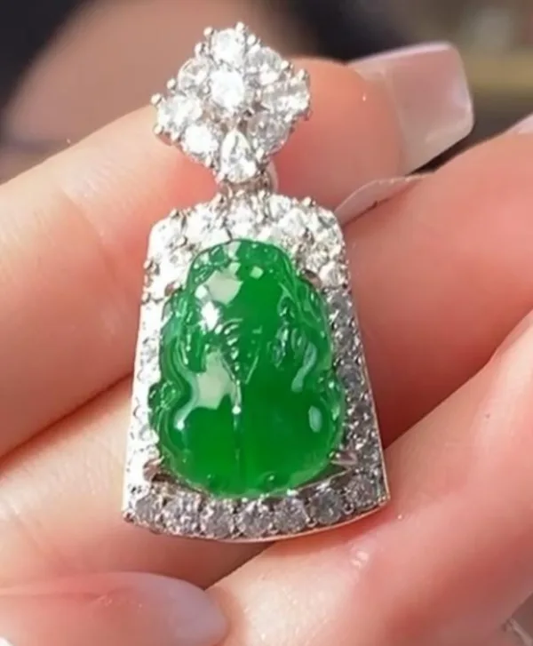 The image displays a meticulously crafted Jadeite Sun Green Pixiu pendant, held between fingers. The pendant is distinguished by its bright green jadeite carving of a Pixiu, a mythical creature associated with wealth, encased in a radiant silver inlay adorned with glittering stones. The combination of the vivid green jade and the sparkling silver creates a piece that is both visually stunning and rich with cultural significance.