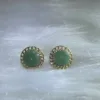 Elegant green jade stud earrings encircled by delicate gold patterns, combining classic beauty with contemporary style.