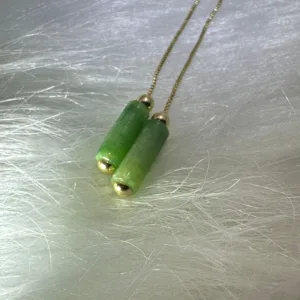 Green cylindrical jade 'Unifying the World' earrings capped with gold, symbolizing cohesive leadership and style.