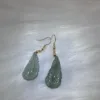 Green leaf-shaped earrings on white surface.