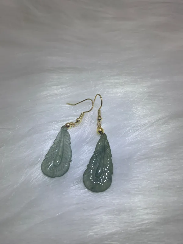 Green leaf-shaped earrings on white surface.