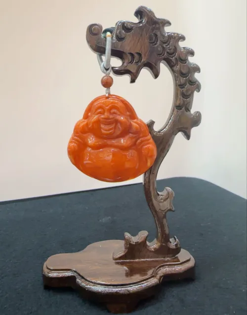 Carved jade Buddha pendant on wooden stand.