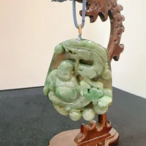 Carved jade Buddha pendant on wooden stand.