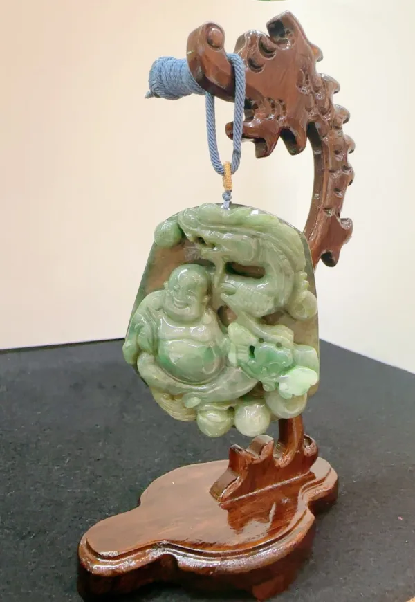 Carved jade Buddha pendant on wooden stand.