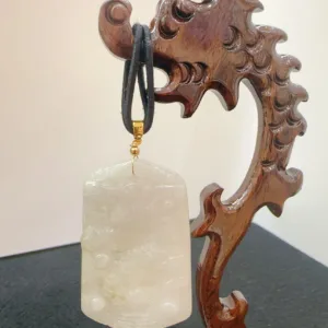 Carved wooden stand displaying jade pendant.