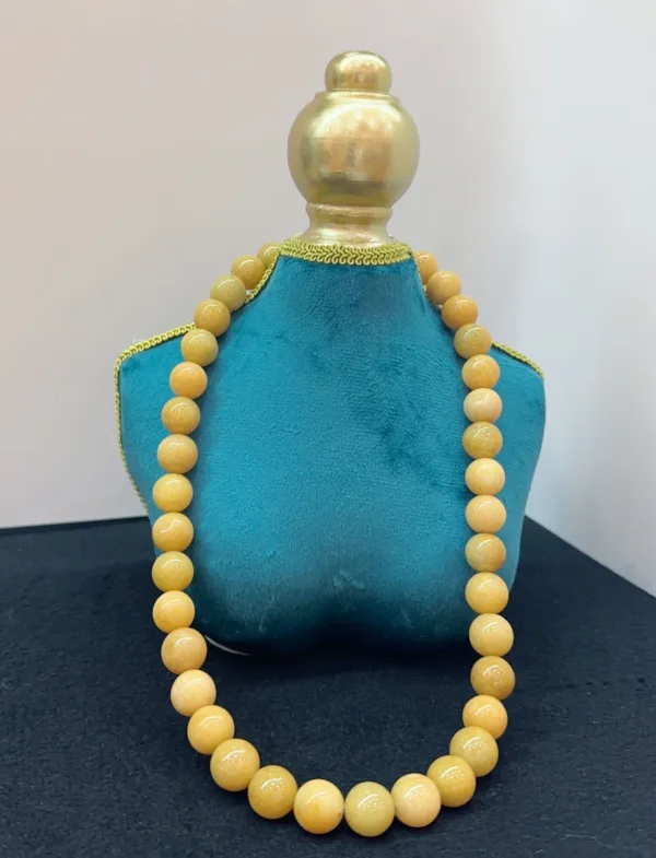 Golden beaded necklace on blue stand.