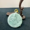 Carved jade Buddha pendant on wooden stand.