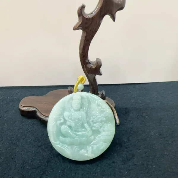Carved jade pendant with Buddha design on wooden stand.