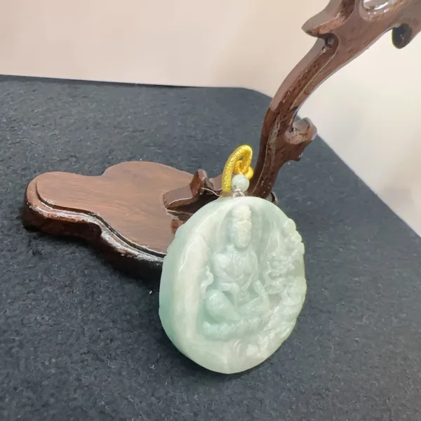 Jade pendant with Buddha carving on wooden stand.
