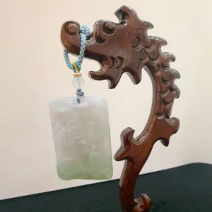 Carved wooden stand displaying a jade pendant.