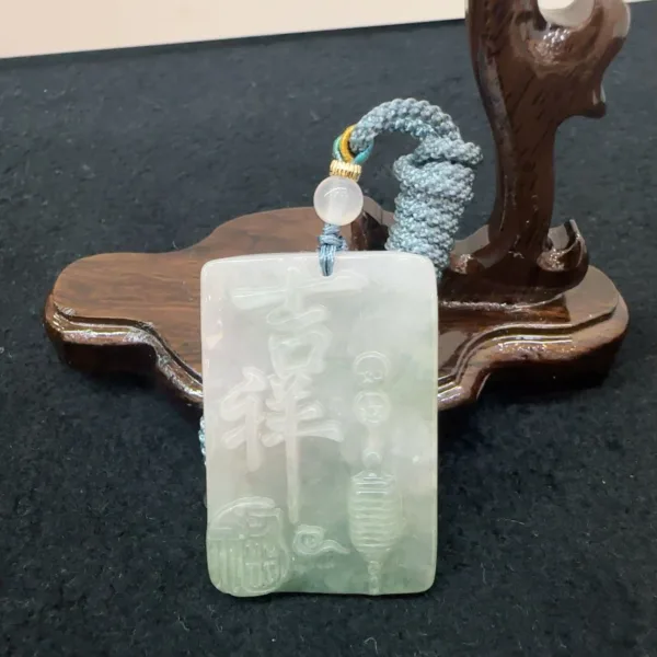 Carved jade pendant on wooden stand.