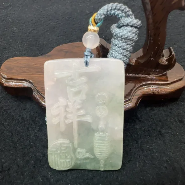 Carved jade pendant with Chinese characters on wooden stand.