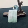 Carved jade pendant on wooden stand.