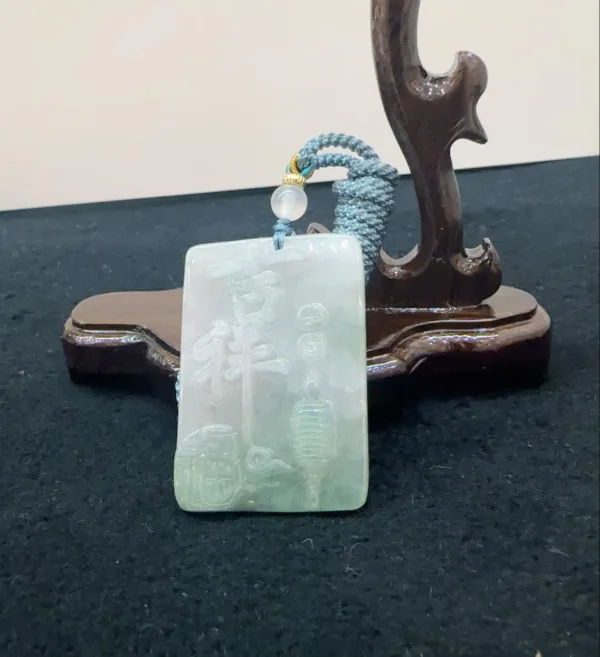 Carved jade pendant on wooden stand.