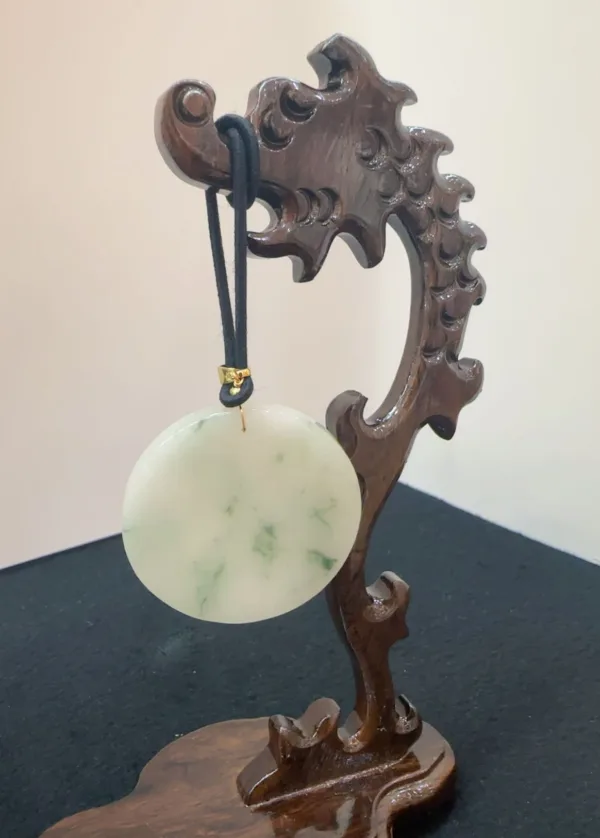 Carved wooden stand holding a jade disc pendant.