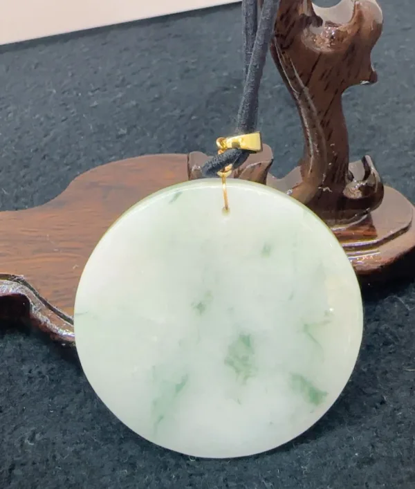 Jade pendant on wooden stand with black cord.