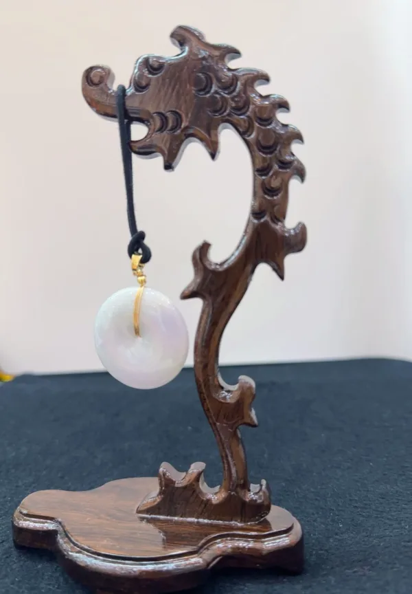 Carved wooden dragon display holding pearl pendant.