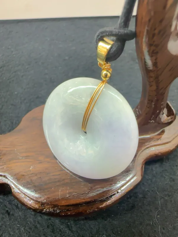 Jade pendant on wooden display stand.