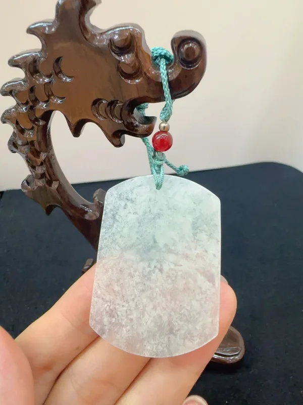 Hand holding a jade pendant with wooden stand.