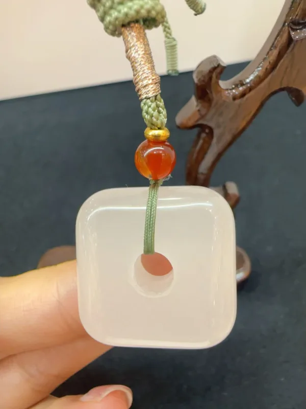 Square jade pendant with bead held by hand.
