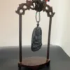 Carved wooden stand displaying a Buddha pendant.
