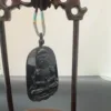 Carved Buddha pendant on wooden stand.