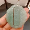 Hand holding intricate jade pendant with traditional carving.