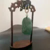 Carved jade pendant on wooden display stand.