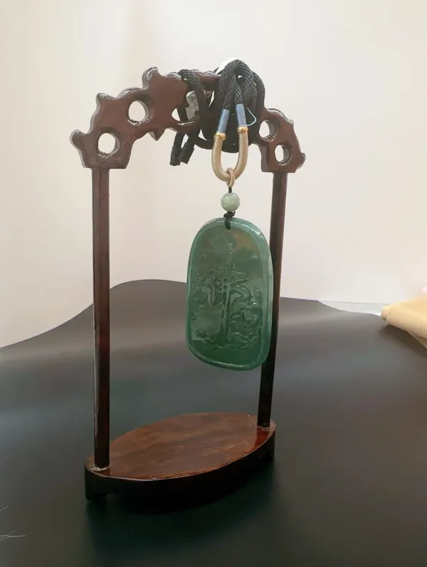 Carved jade pendant on wooden display stand.