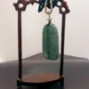 Carved jade pendant on wooden stand.