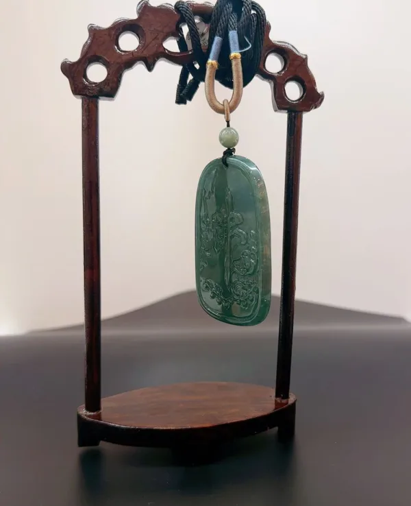 Carved jade pendant on wooden stand.