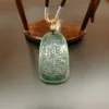 Carved jade pendant on wooden stand.