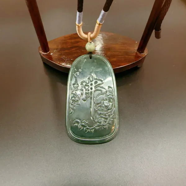 Carved jade pendant on wooden stand.