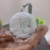 Carved jade ornament on wooden base with greenery.