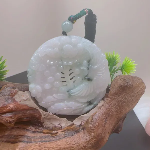 Carved jade ornament on wooden base with greenery.