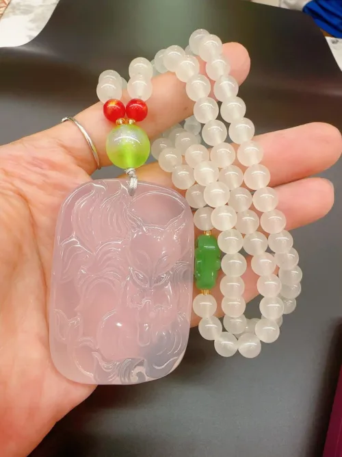 Hand holding carved jade dragon pendant and beads.