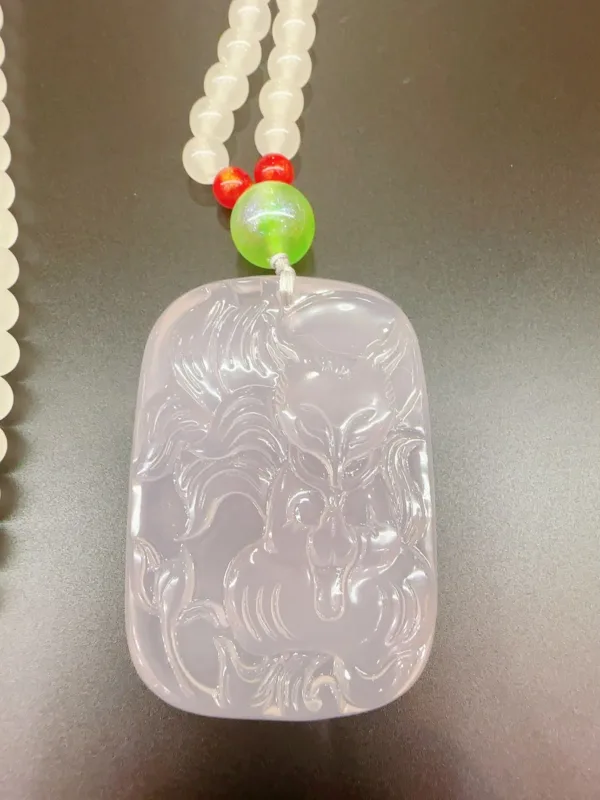 Carved jade pendant with beads on table.