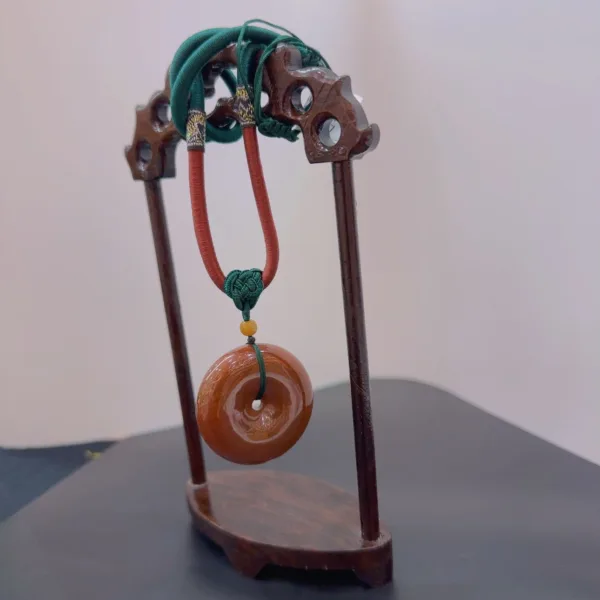 Carved wooden stand displaying a jade pendant.