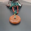 Orange donut pendant with green cord.