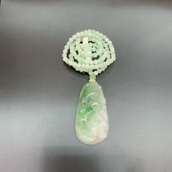 Jade pendant with beaded necklace on grey background.