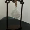 Carved jade ornament on wooden stand with rope.