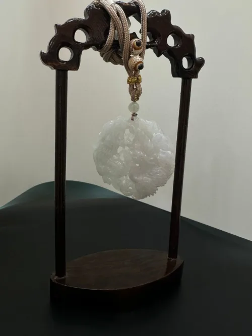 Carved jade ornament on wooden stand with rope.