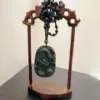 Carved jade pendant on wooden stand with beads.