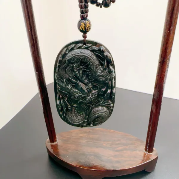 Carved jade dragon pendant on wooden stand.