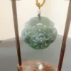 Carved jade pendant with floral design on display stand.