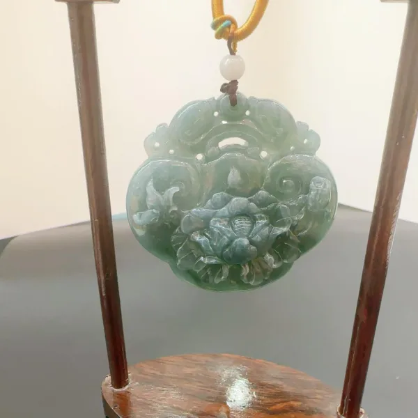 Carved jade pendant with floral design on display stand.