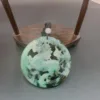 Carved jade pendant on wooden display stand.